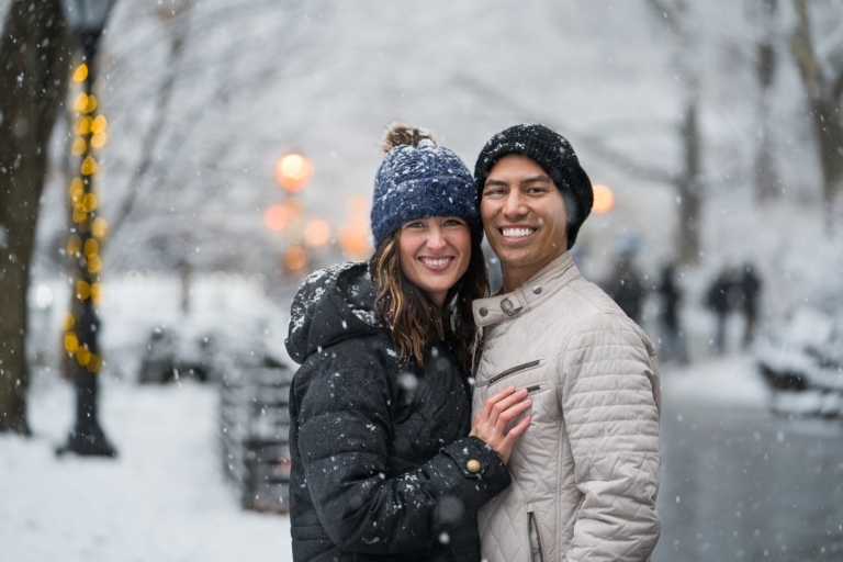 Couple smiles while embracing in a snowy park.