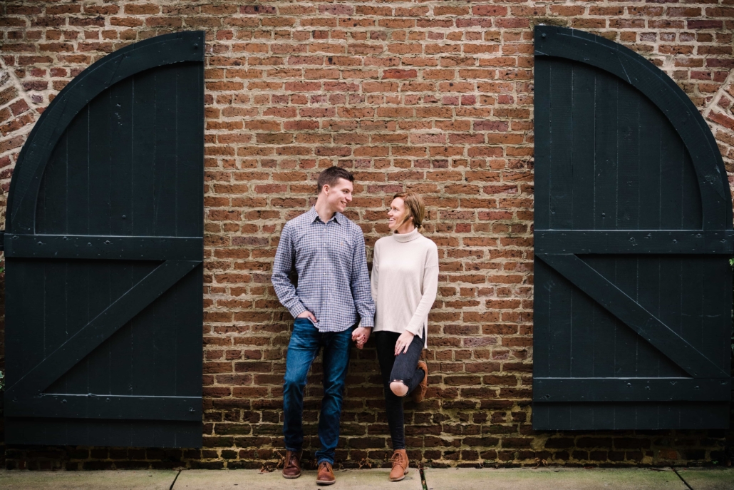 Engaged couple leans against a wall and looks at each other