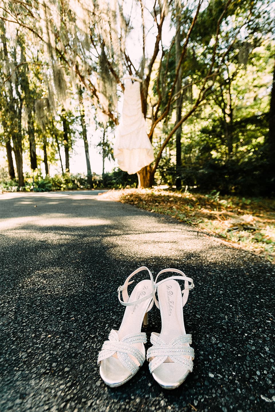 brides shoes are displayed while her dress hangs in a tree
