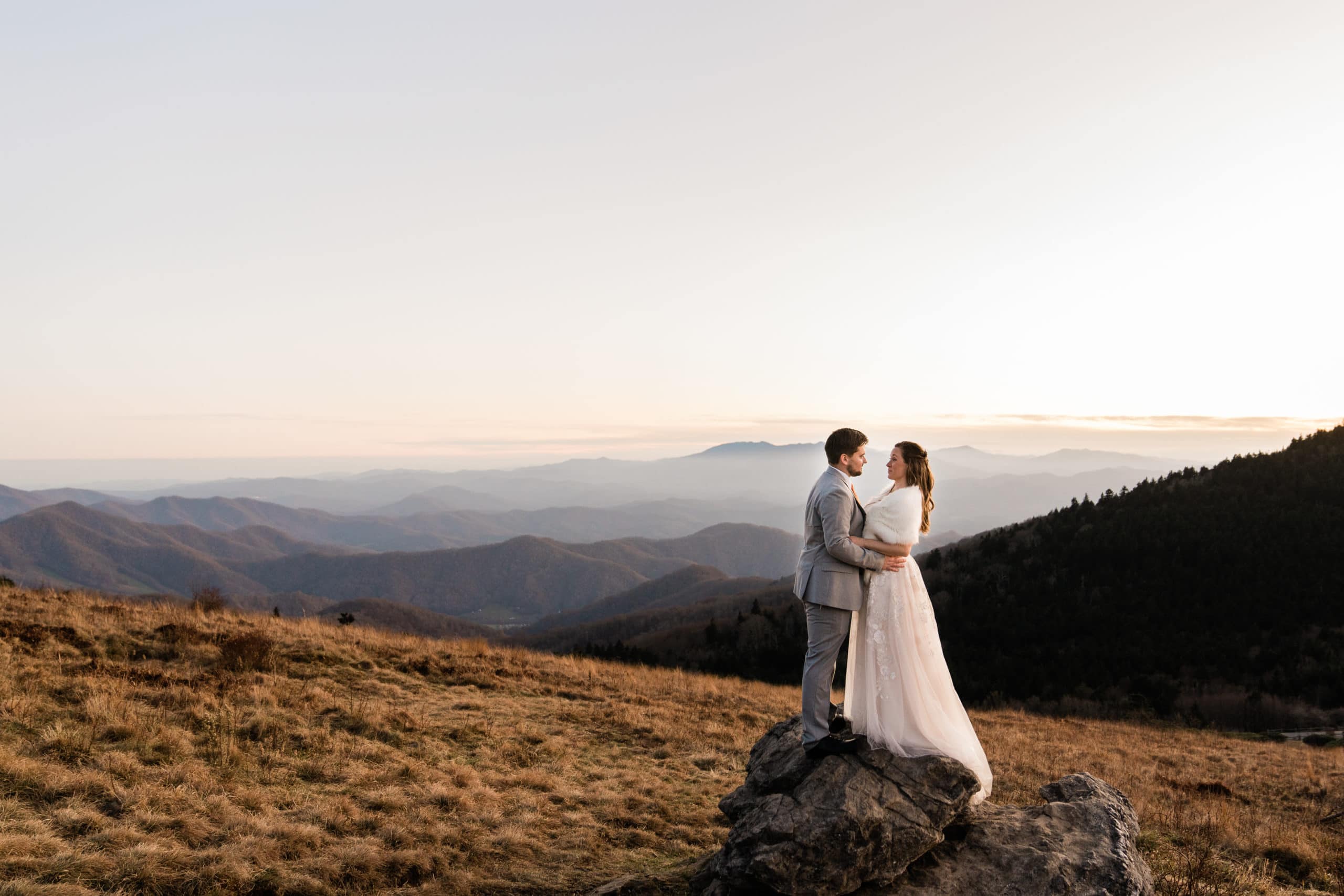 couple embraces on a rock with beautiful mountain views in the background