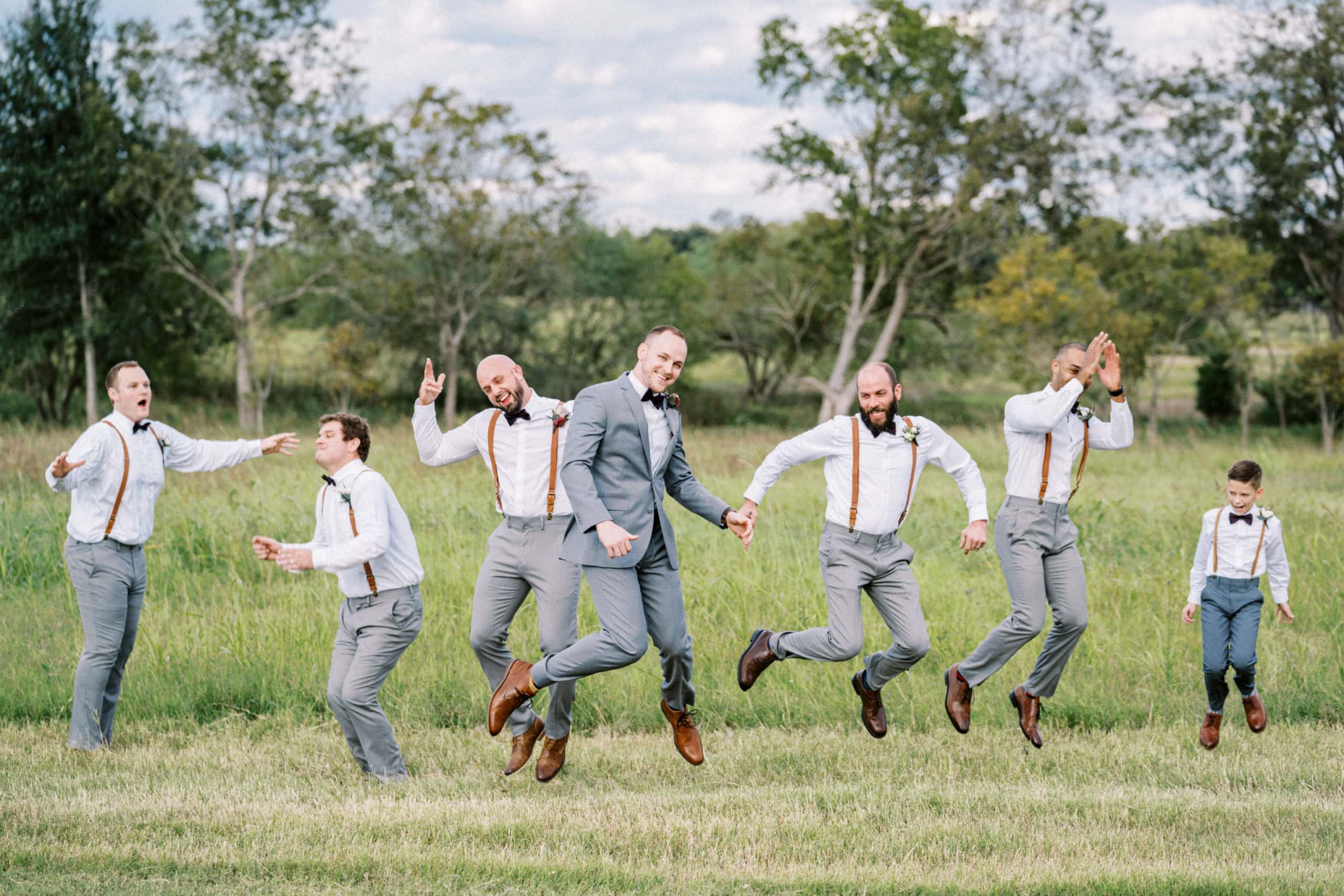 Groom and groomsmen jump together in a field