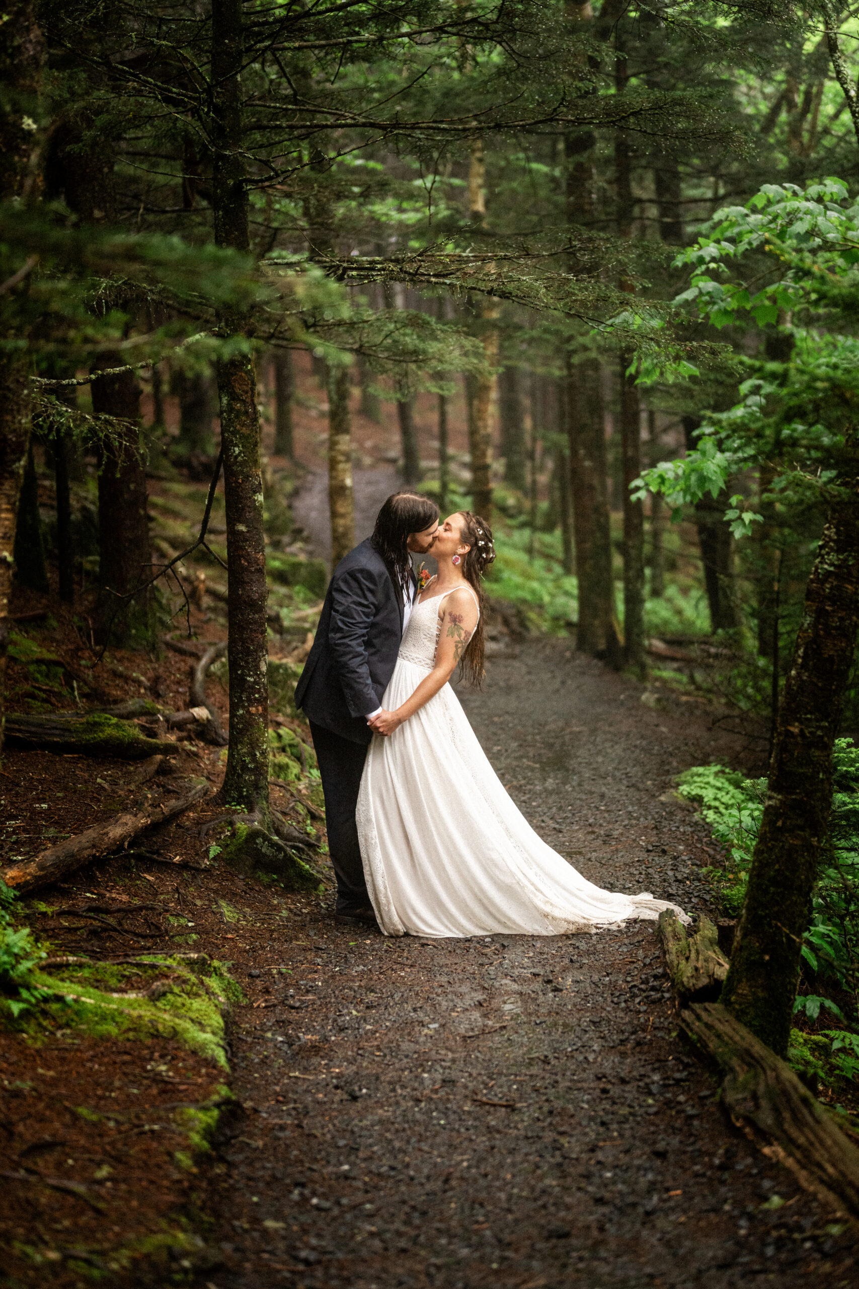 Bride and groom kiss passionately in the forest while rain falls around them