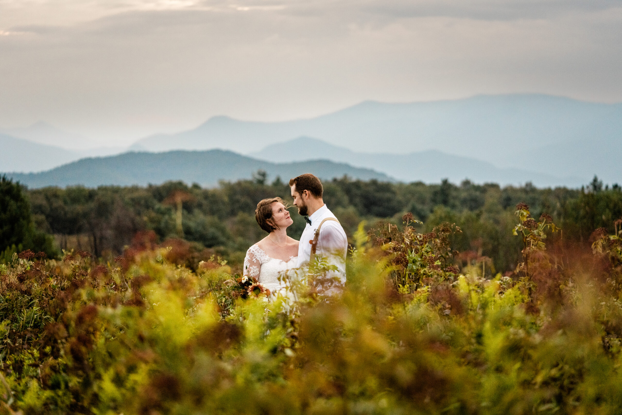Bride and Groom stare into each others eyes in a field with tall flowers and mountains in the background