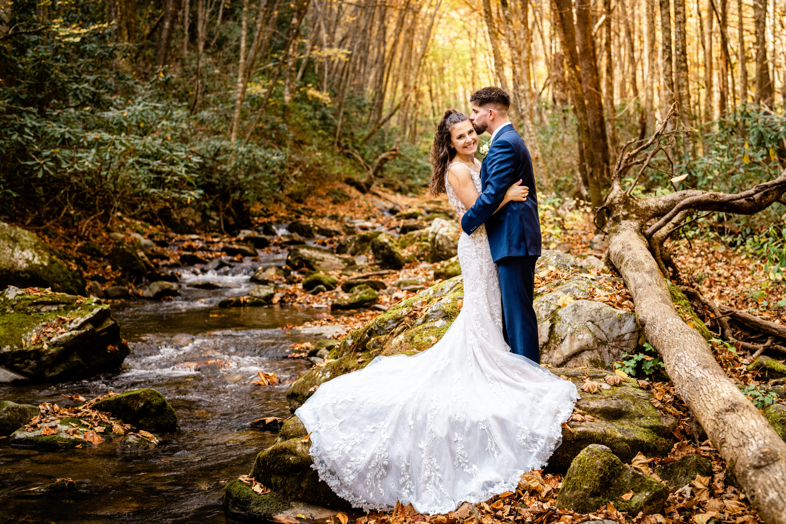 Bride and Groom embrace on a rock in the middle of a beautiful creek during fall